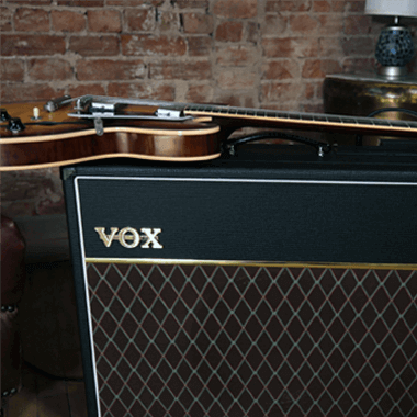 electric guitar lying on top of VOX amplifier in front of brick wall