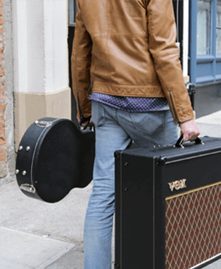 partial view of person carrying VOX amplifier in one hand and guitar case in other hand