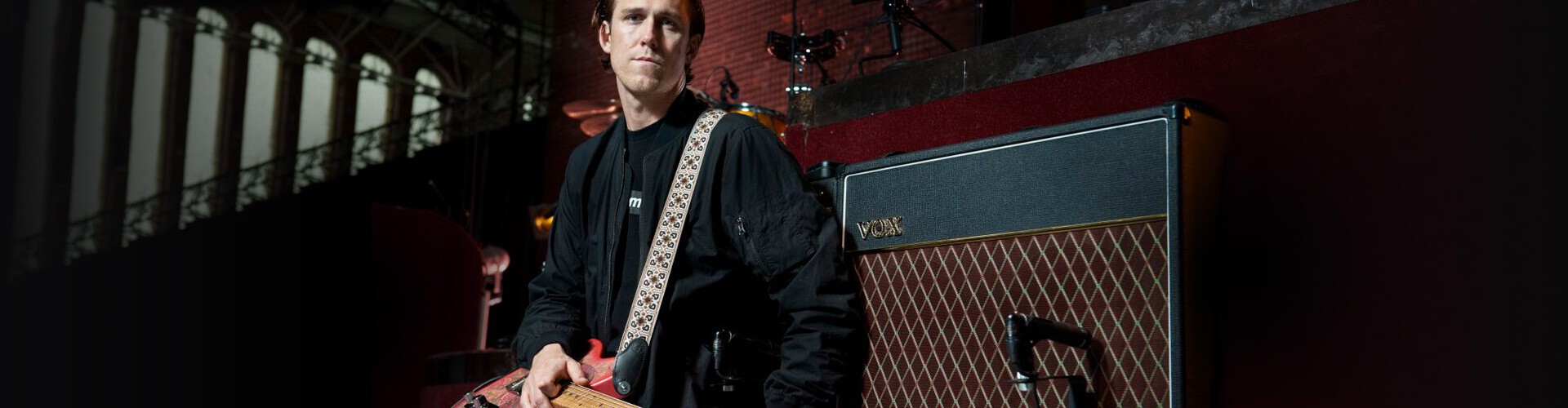 artist, Rob Ackroyd, holding electric guitar standing next to VOX amplifier