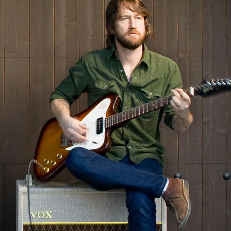 musician, Nate Mendel. playing electric guitar and sitting on VOX amplifier