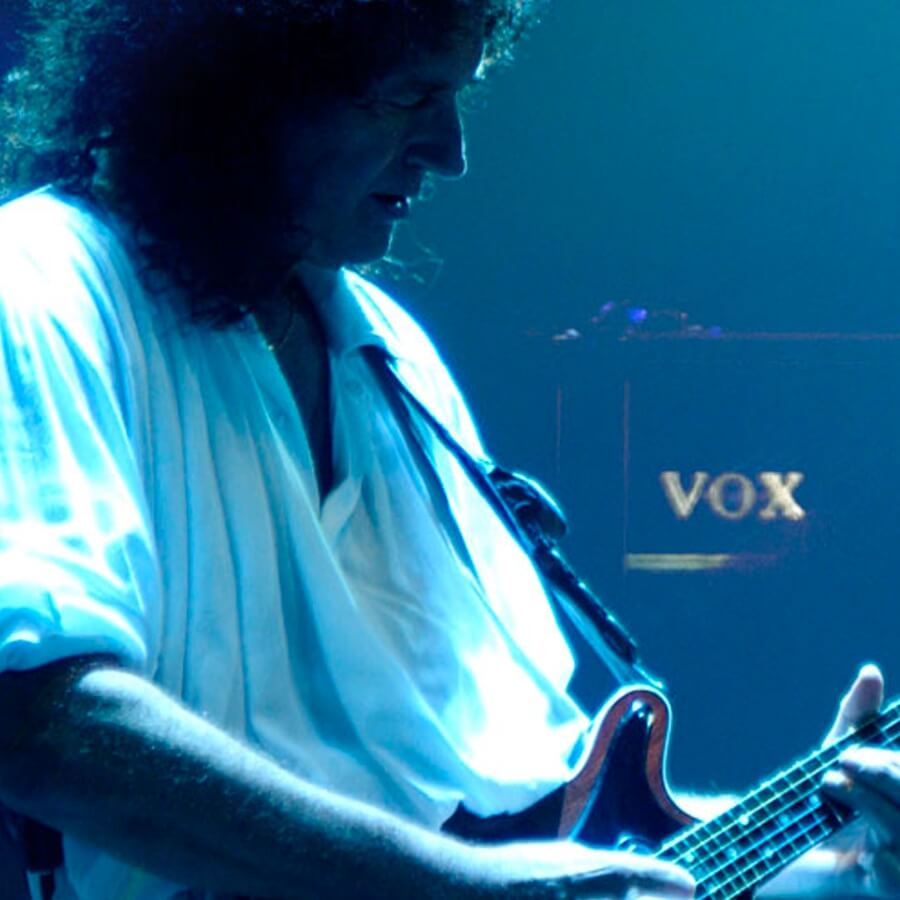 Musician, Brian May, playing electric guitar with a VOX amplifier behind him