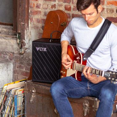 Vox Cambridge50 guitar modeling amp sitting on a trunk to the left of a man playing an electric guitar