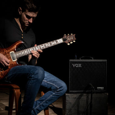 Vox Cambridge50 guitar modeling amp sitting to the right of a man playing an electric guitar