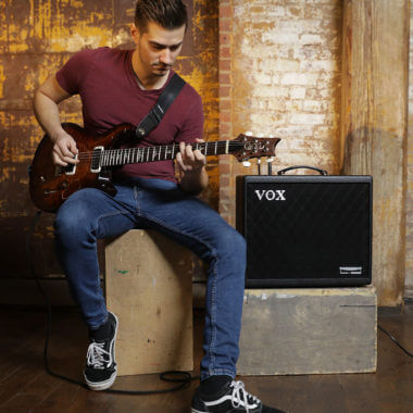 Vox Cambridge50 guitar modeling amp sitting to the right of a man playing an electric guitar