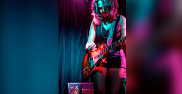 female musician playing electric guitar in front of VOX amplifier