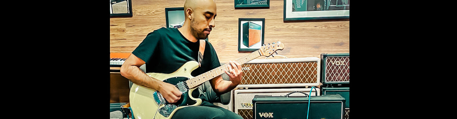 male musician playing electric guitar in front of VOX amplifiers