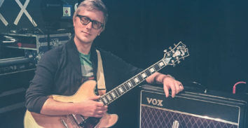 male musician holding electric guitar beside VOX amplifier
