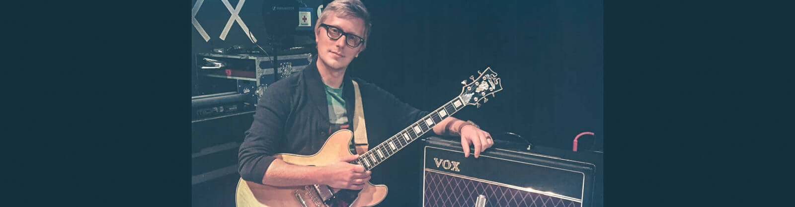 male musician holding electric guitar beside VOX amplifier