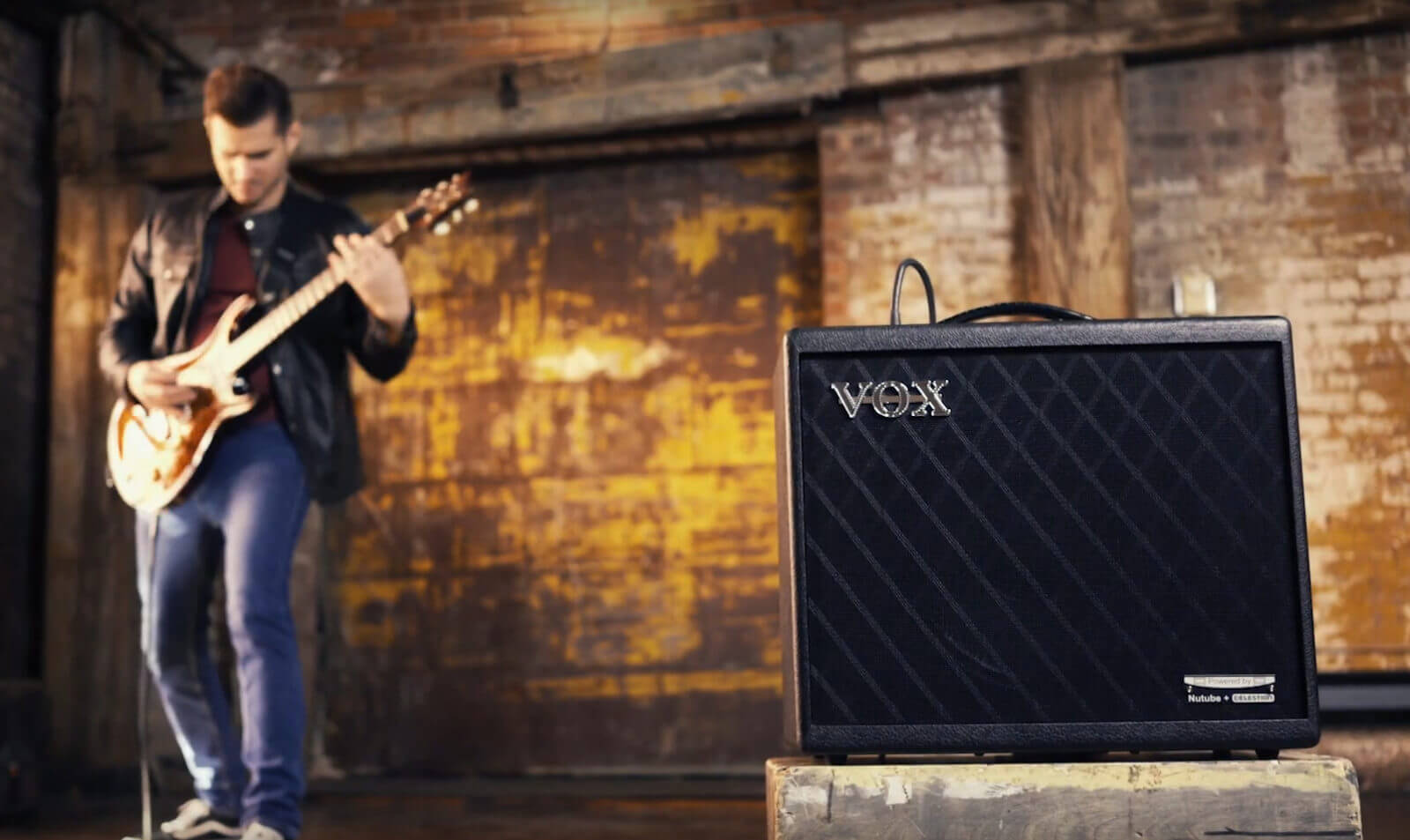 man playing electric guitar behind VOX amplifier