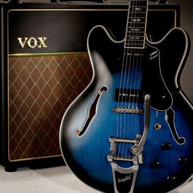 body of black and blue electric guitar in front of amplifier