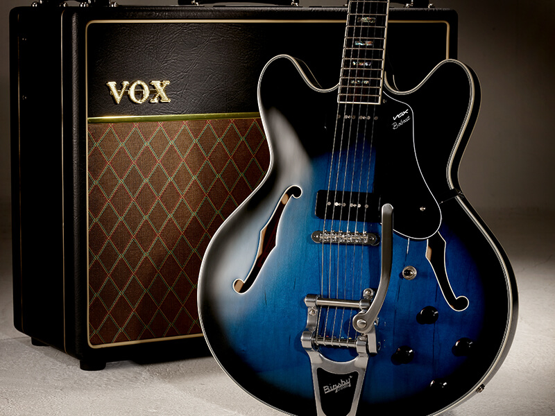body of black and blue electric guitar in front of amplifier