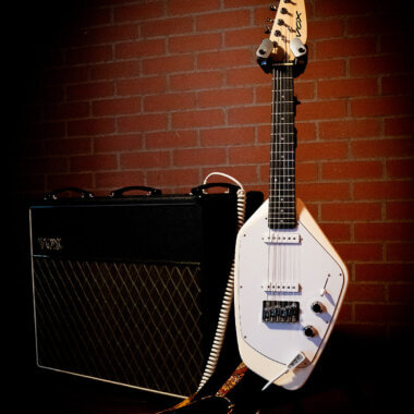 Vox Mark V Mini Guitar white on stand besides Vox amplifier.
