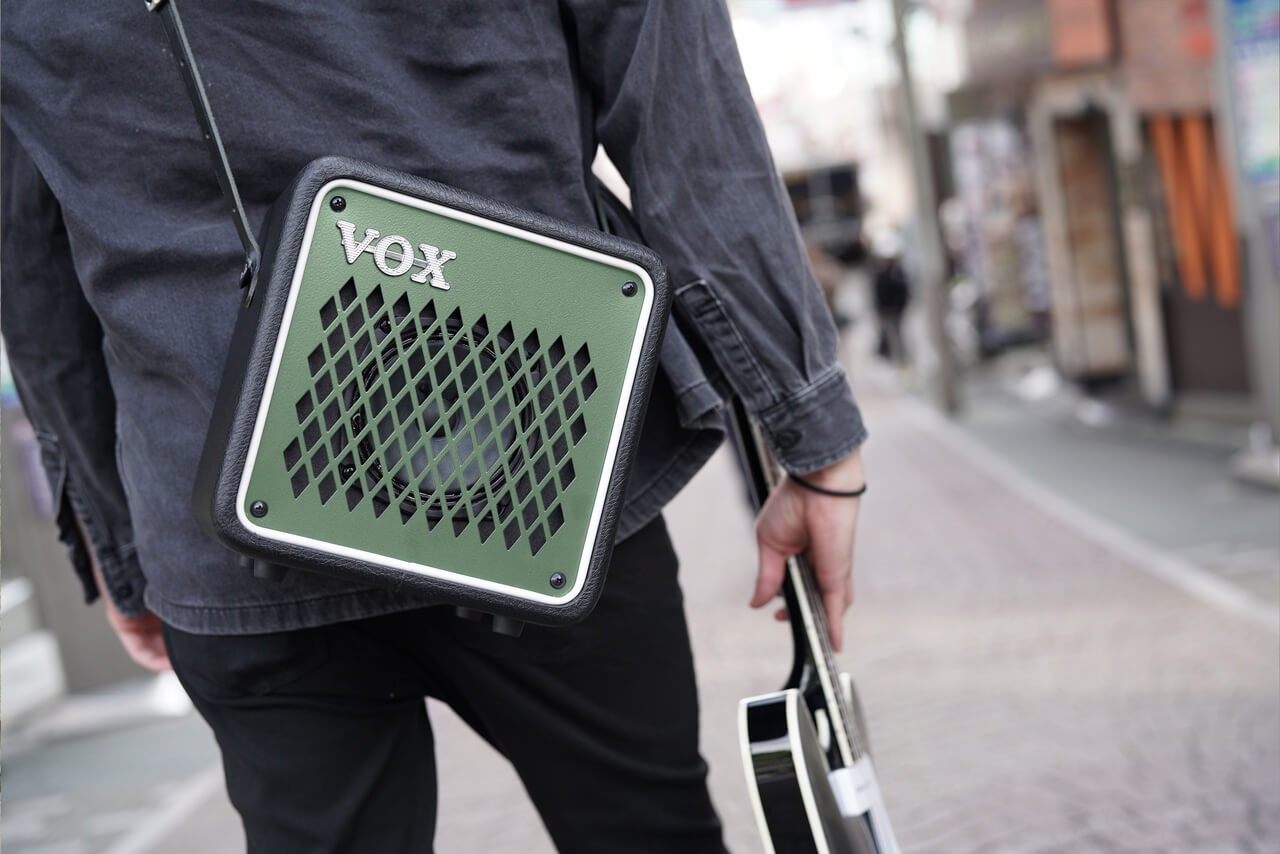 Vox mini go 10 olive green with sling hang on the back of an artist holding guitar.