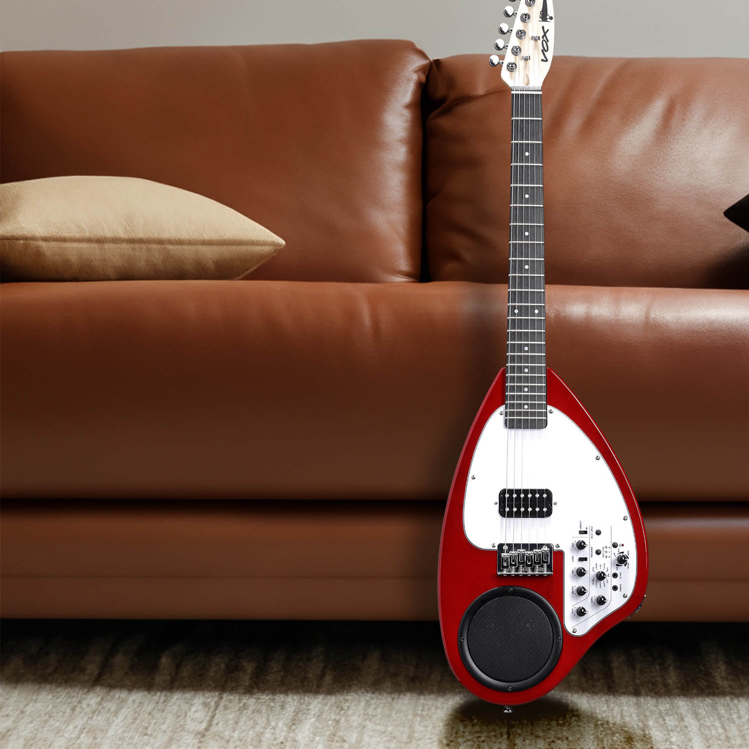 VOX APC-1 mini guitar in red leaning against brown leather sofa