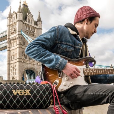 man playing electric guitar and using VOX AudioAir GT beside the Tower Bridge in London