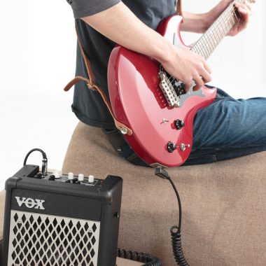man playing red electric guitar beside VOX mini amplifier